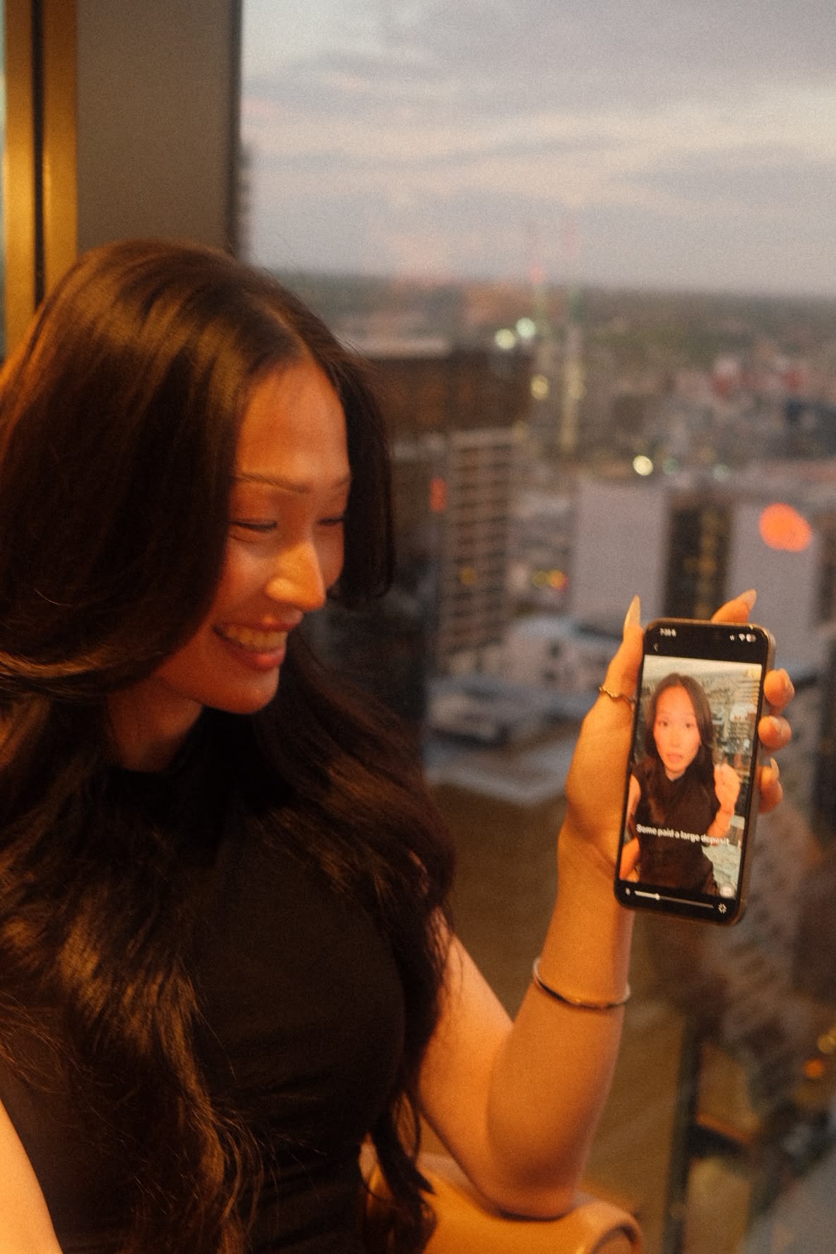 A woman holding a phone beside a window overlooking the city during a Simvera Legal personal branding shoot